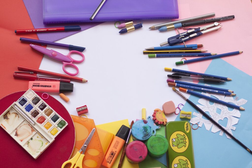 diversos materiais escolares como lápis, tesoura, tinta guache, marcador de texto, apontador, borracha, sobre papéis coloridos